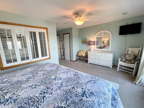 Quarto com cama, penteadeira, cadeira e ventoinha no teto.
