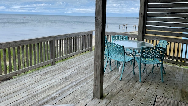 Une terrasse en bois avec une table en verre et des chaises turquoise, offrant une vue sur l’océan.