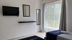 Habitación de hotel con dos camas, un televisor, un espejo, una ventana con cortinas y una repisa.