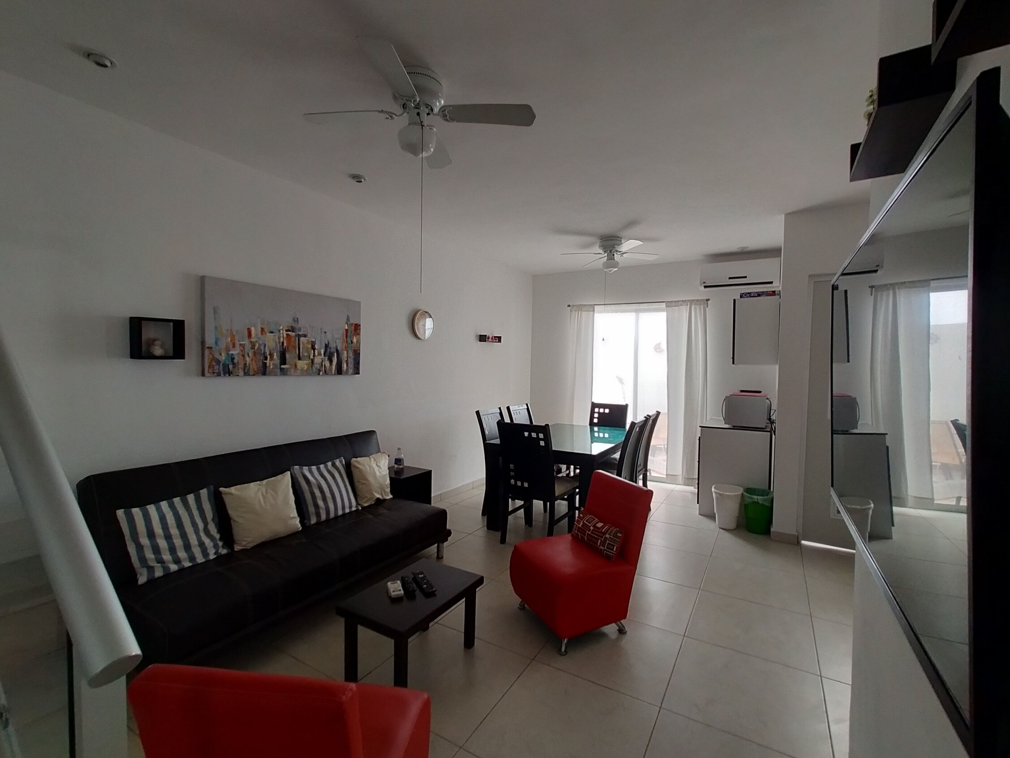 A modern living room with a black sofa, red armchair, and a dining area with a table and chairs.