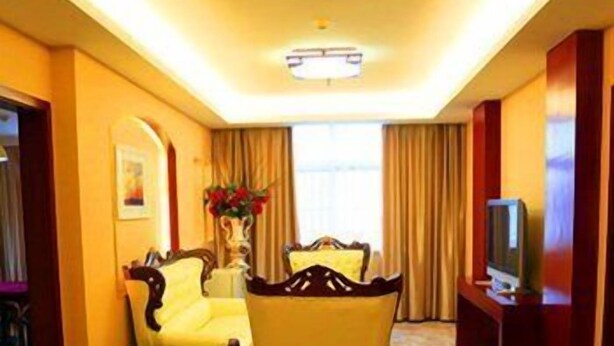 A hotel room with a large bed, a sitting area with a sofa and armchairs, a television, and a window with curtains. - Greentree Alliance Hotel (Suzhou)
