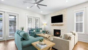 A modern living room with a fireplace, two sofas, a coffee table, and a TV mounted on the wall. - Seacrest Beach Home + Dog Friendly, Tram & Bikes (Seacrest Beach)