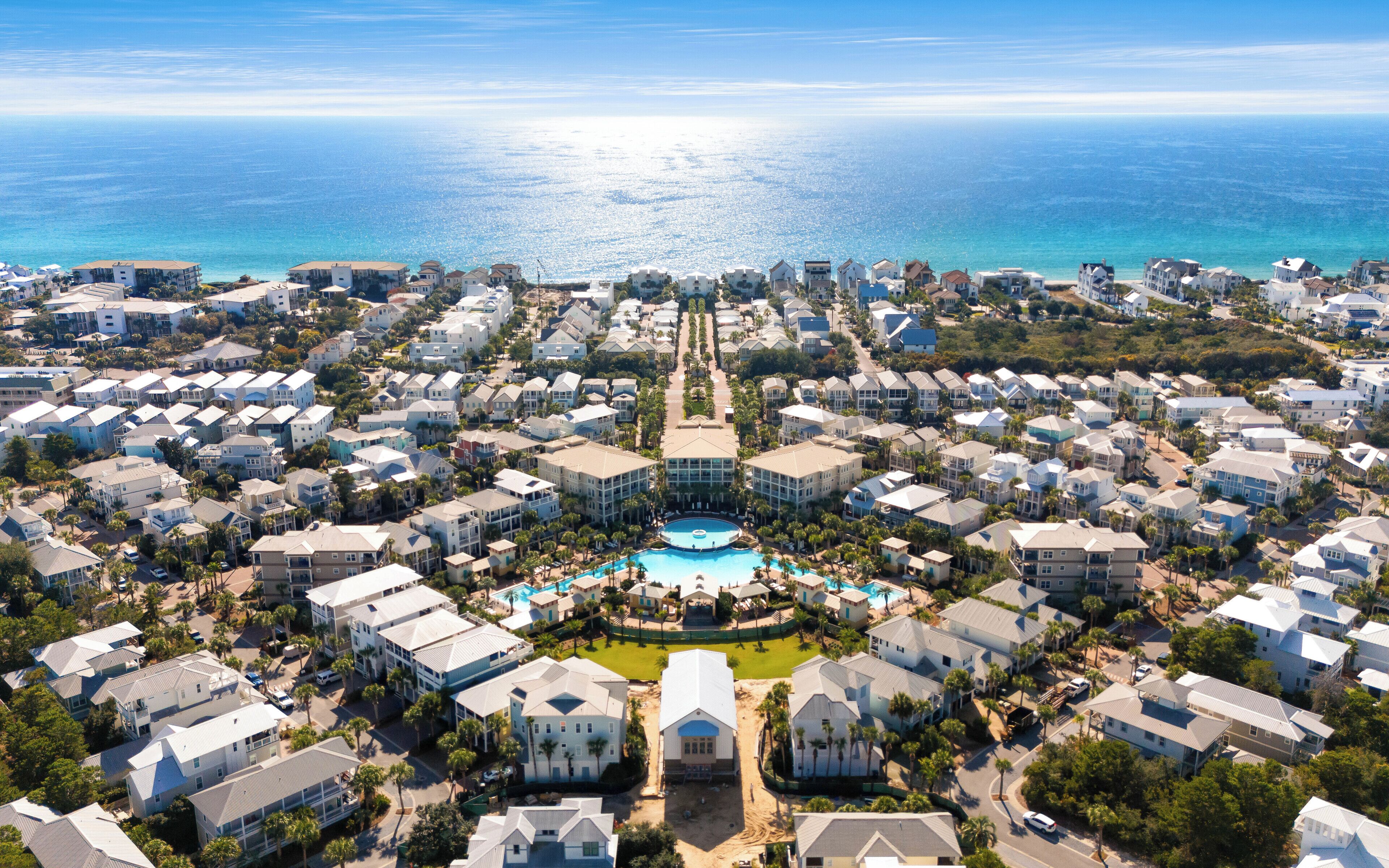 An aerial view of a coastal residential area with a central swimming pool surrounded by houses.