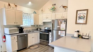 A modern kitchen with white cabinets, stainless steel appliances, and decorative wall art. - Blue Crab:  Spacious screened porch, short stroll to Ocracoke Coffee Co.. (Ocracoke)