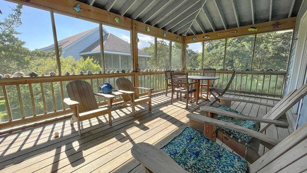 A covered outdoor deck with wooden furniture, a ceiling fan, and a view of a house and trees. - Blue Crab:  Spacious screened porch, short stroll to Ocracoke Coffee Co.. (Ocracoke)