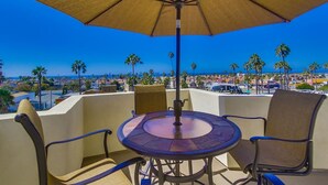 A balcony with a table and chairs, an umbrella, and a view of a coastal cityscape. - Spanish Town home Just Blocks To The Beach With Panoramic Ocean Views (Oceanside)