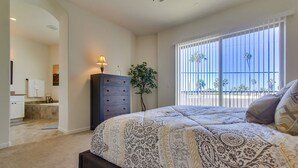 A bedroom with a large bed, a dresser, a nightstand, a lamp, and a window with a view of palm trees. - Spanish Town home Just Blocks To The Beach With Panoramic Ocean Views (Oceanside)