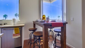 A kitchen with a wooden table, stools, and a window with a view of palm trees. - Spanish Town home Just Blocks To The Beach With Panoramic Ocean Views (Oceanside)