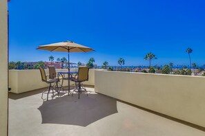 A balcony with a table and chairs, an umbrella, and a view of palm trees and buildings.