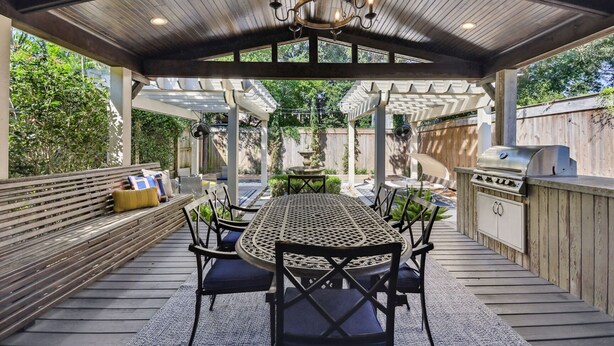 Een terras buiten met een ronde tafel, stoelen, een barbecue en een pergola.