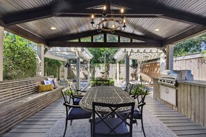 An outdoor patio with a round table, chairs, a grill, and a pergola structure.