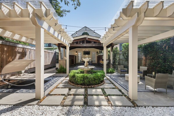 A covered patio area with a central fountain, outdoor seating, and a pergola structure.