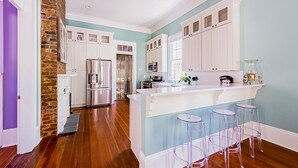 Een moderne keuken met witte kasten, een roestvrijstalen koelkast, een bar met krukken en uitzicht op de eetruimte.