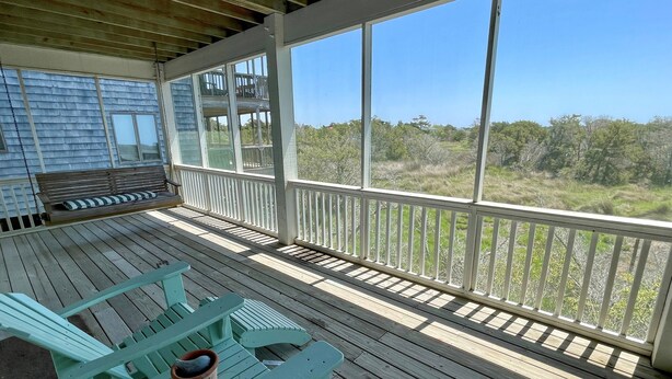 A covered deck with wooden flooring and white railings, featuring a bench and chairs, and a view of a natural landscape. - Sea View: Rooftop deck with spectacular views. (Ocracoke)