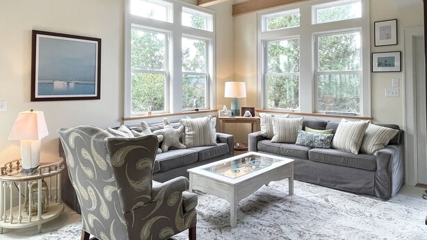 A living room with a sofa set, a coffee table, and a lamp. There are large windows providing natural light. - Safe Harbor:  Expansive views of the salt marsh, maritime forest. (Ocracoke)
