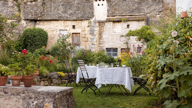 Un espacio al aire libre para comer con mesas y sillas, rodeado de macetas con plantas y flores.