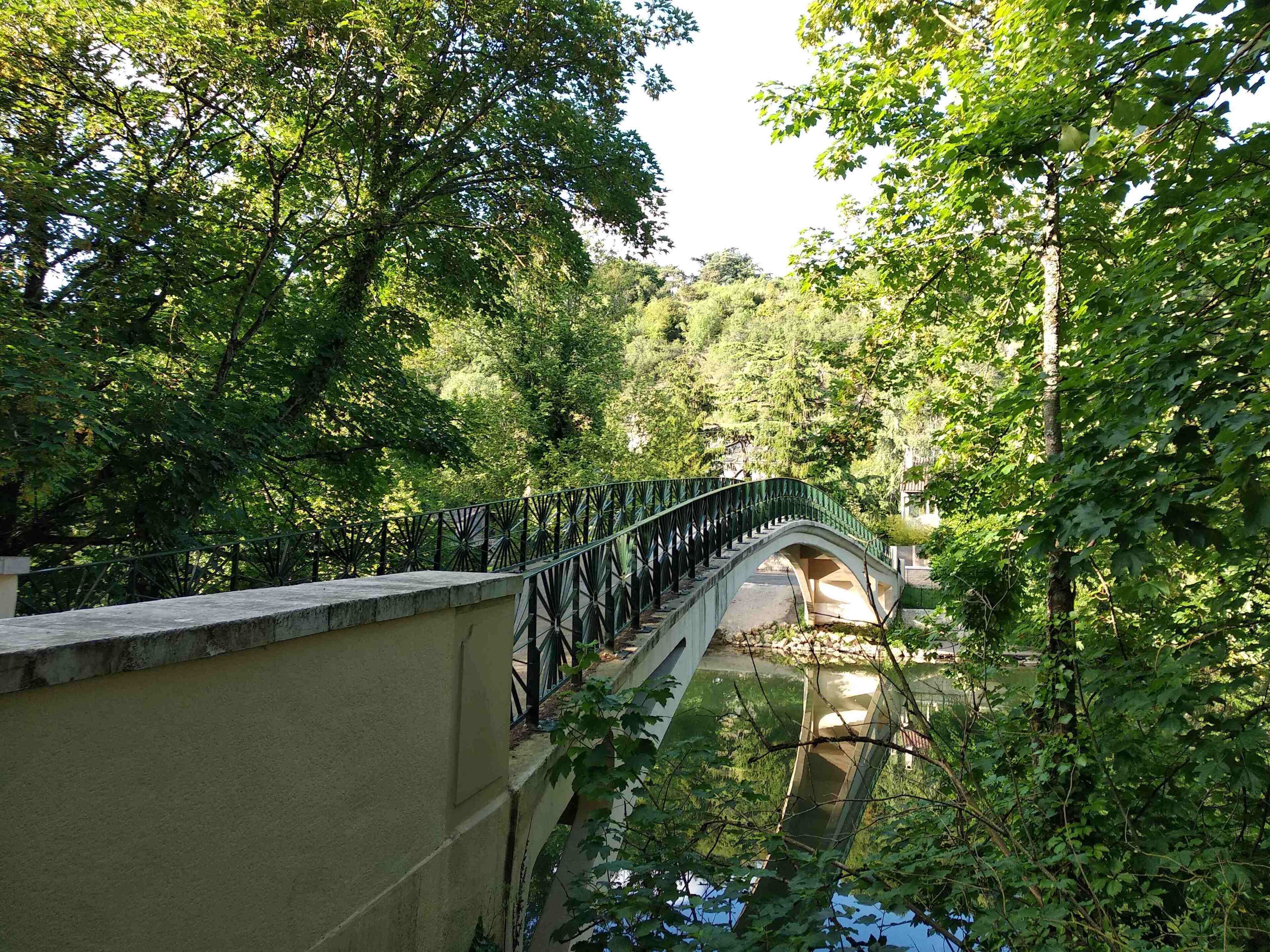 A stone bridge with metal railings, surrounded by lush green trees.