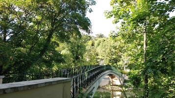A stone bridge with metal railings, surrounded by lush green trees.