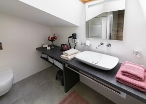 A modern bathroom with a white sink, black countertop, and a mirror above it. There are towels and a small vase with flowers on the countertop. - Clos des Moulins (Poitiers)