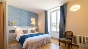 Un dormitorio con una cama grande, una silla, un radiador y una ventana con cortinas.