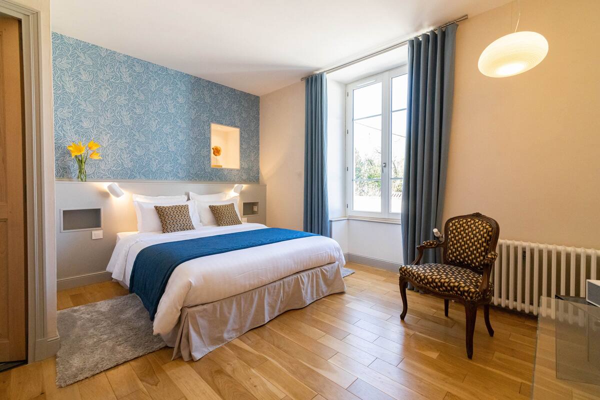 A bedroom with a large bed, a chair, a radiator, and a window with curtains.
