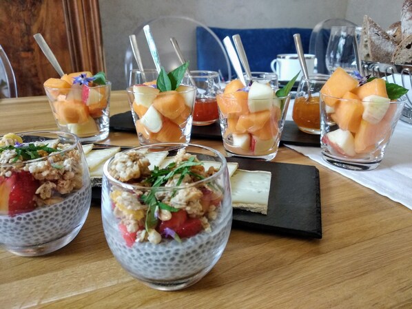 Una mesa con diversas frutas y postres, incluyendo un pudin de chía coronado con fresas y nueces, y vasos con trozos de melón y manzana.