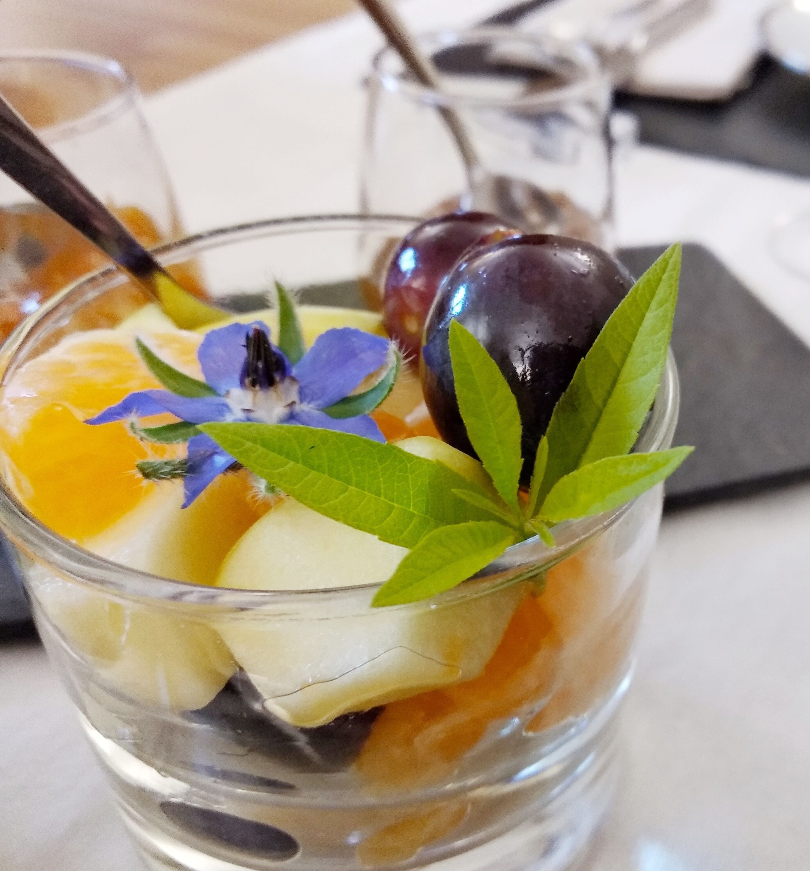 A clear glass with a layered drink, garnished with a blue flower and green leaves.