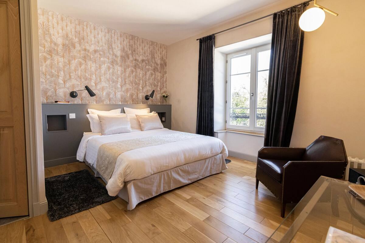 A bedroom with a bed, a chair, a window, and a lamp.