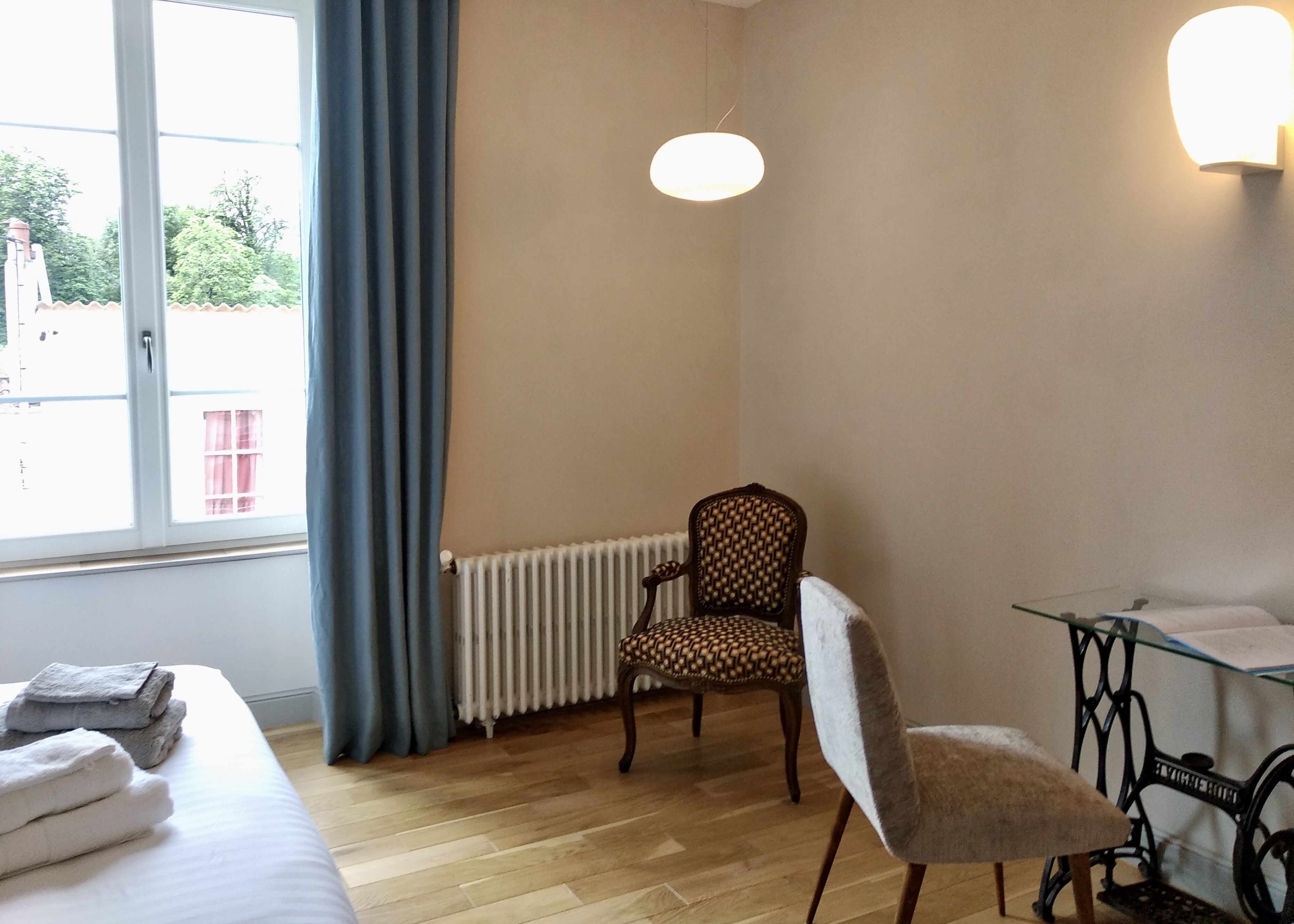 A room with a bed, a chair, a table, a radiator, and a window with curtains.