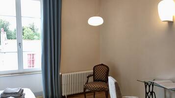 A room with a bed, a chair, a table, a radiator, and a window with curtains.