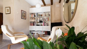 Una sala de estar con dos sillones blancos, una estantería blanca y un televisor.