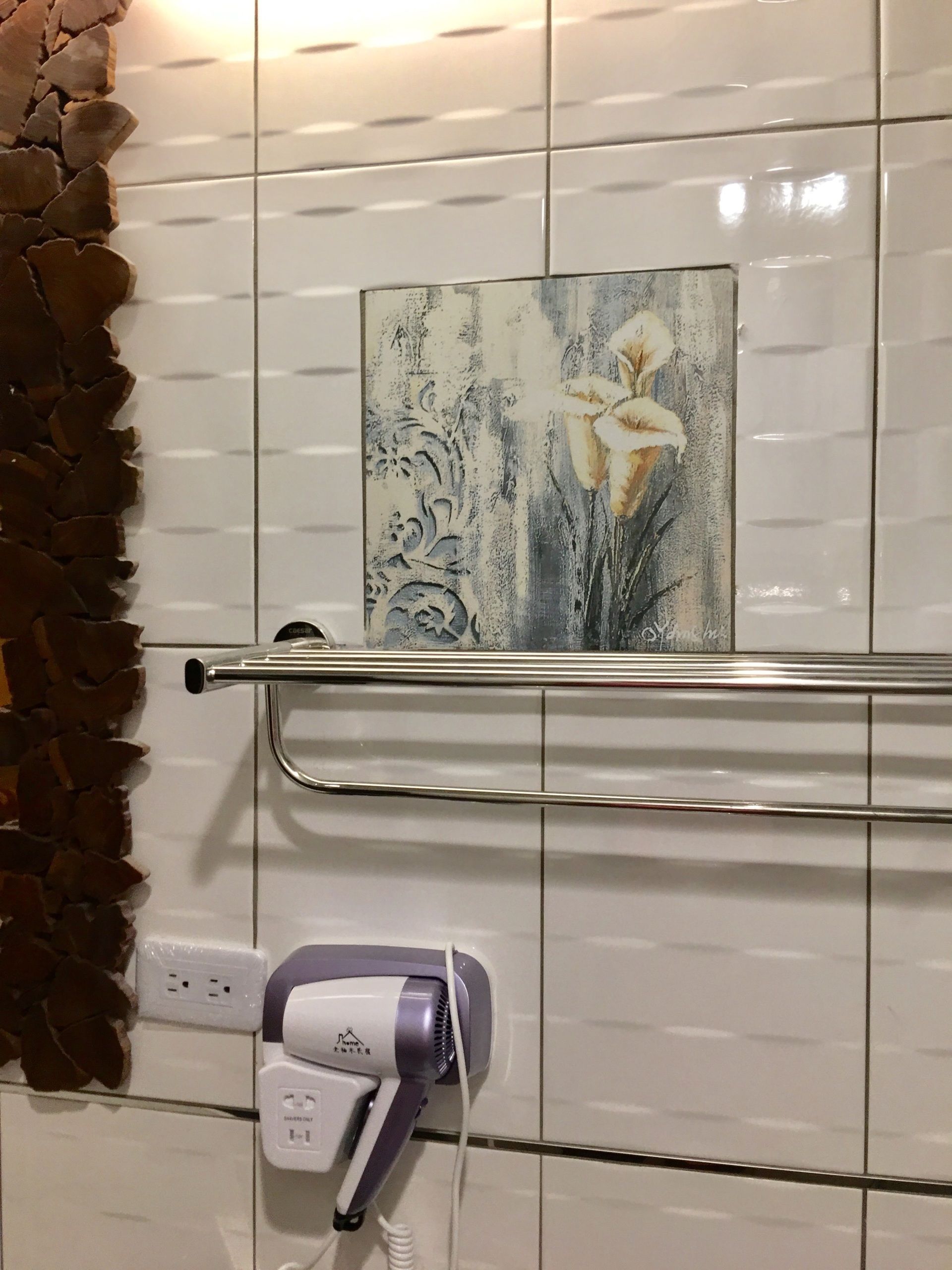 Un baño con azulejos blancos, barandilla, toma de corriente y secador de pelo.