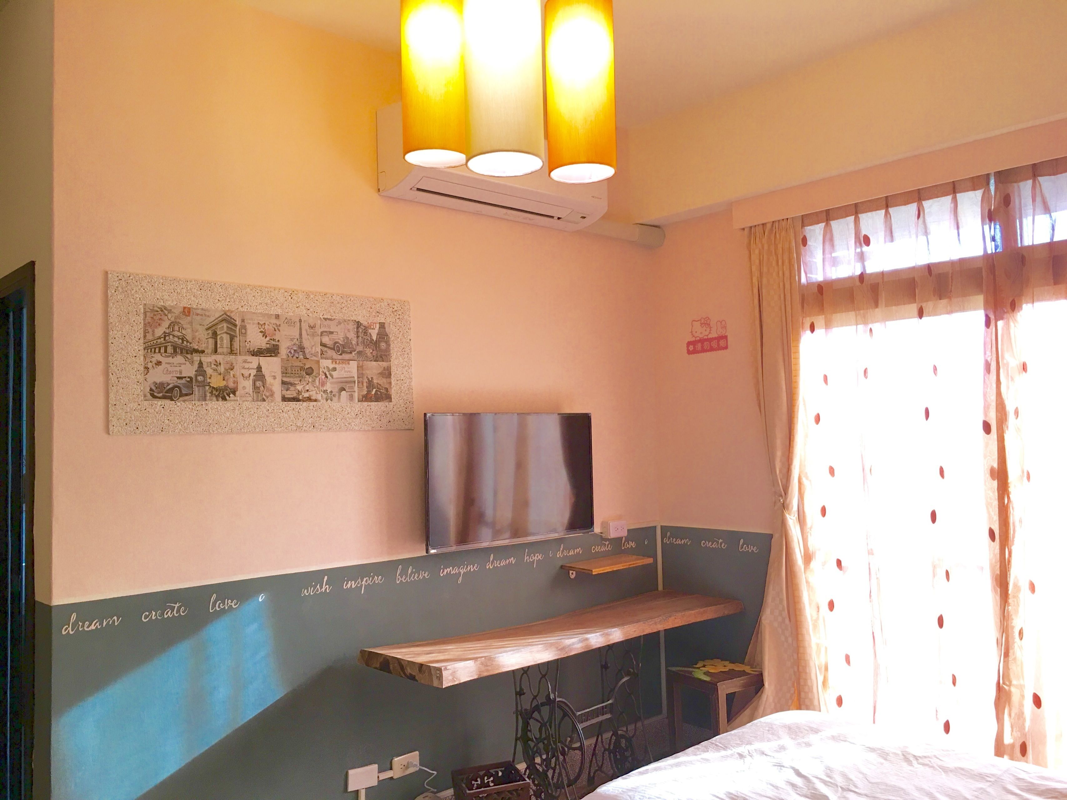 A bedroom with a bed, a mounted TV, a wall-mounted air conditioner, a framed collage, and a window with curtains.