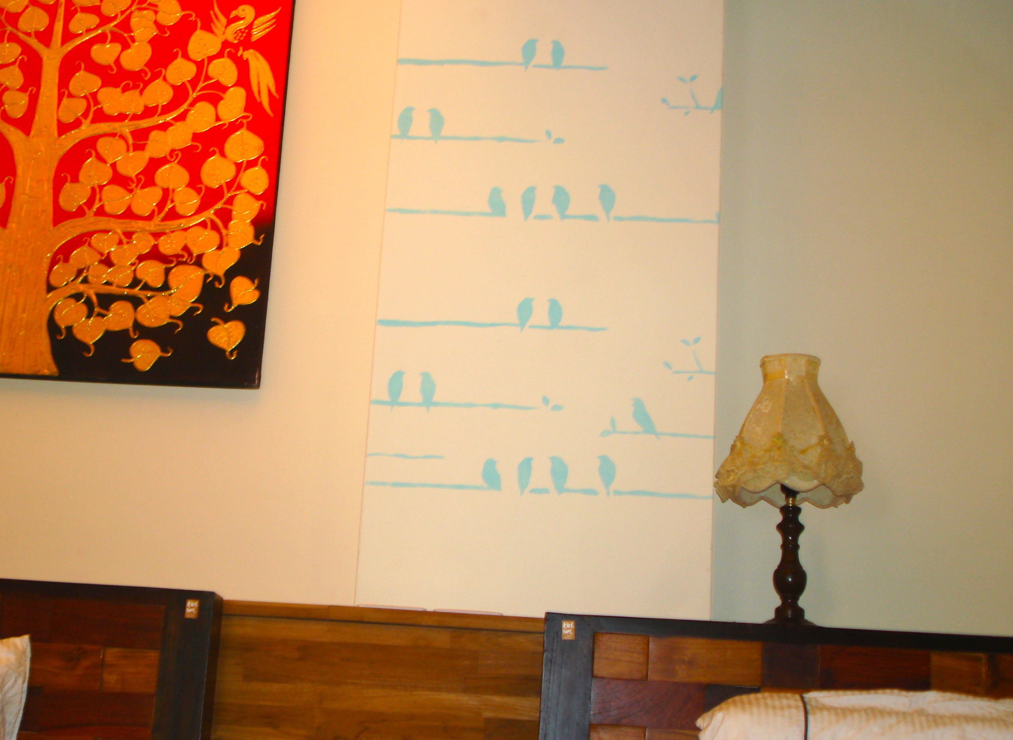 A room with a wooden headboard, a wall with a bird pattern, and a lamp.