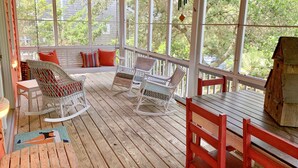 A covered porch with wicker rocking chairs, a wooden table, and a bench with colorful cushions. - Fresh Fruit:  Pet Friendly, pleasant single story on private lane. (Ocracoke)