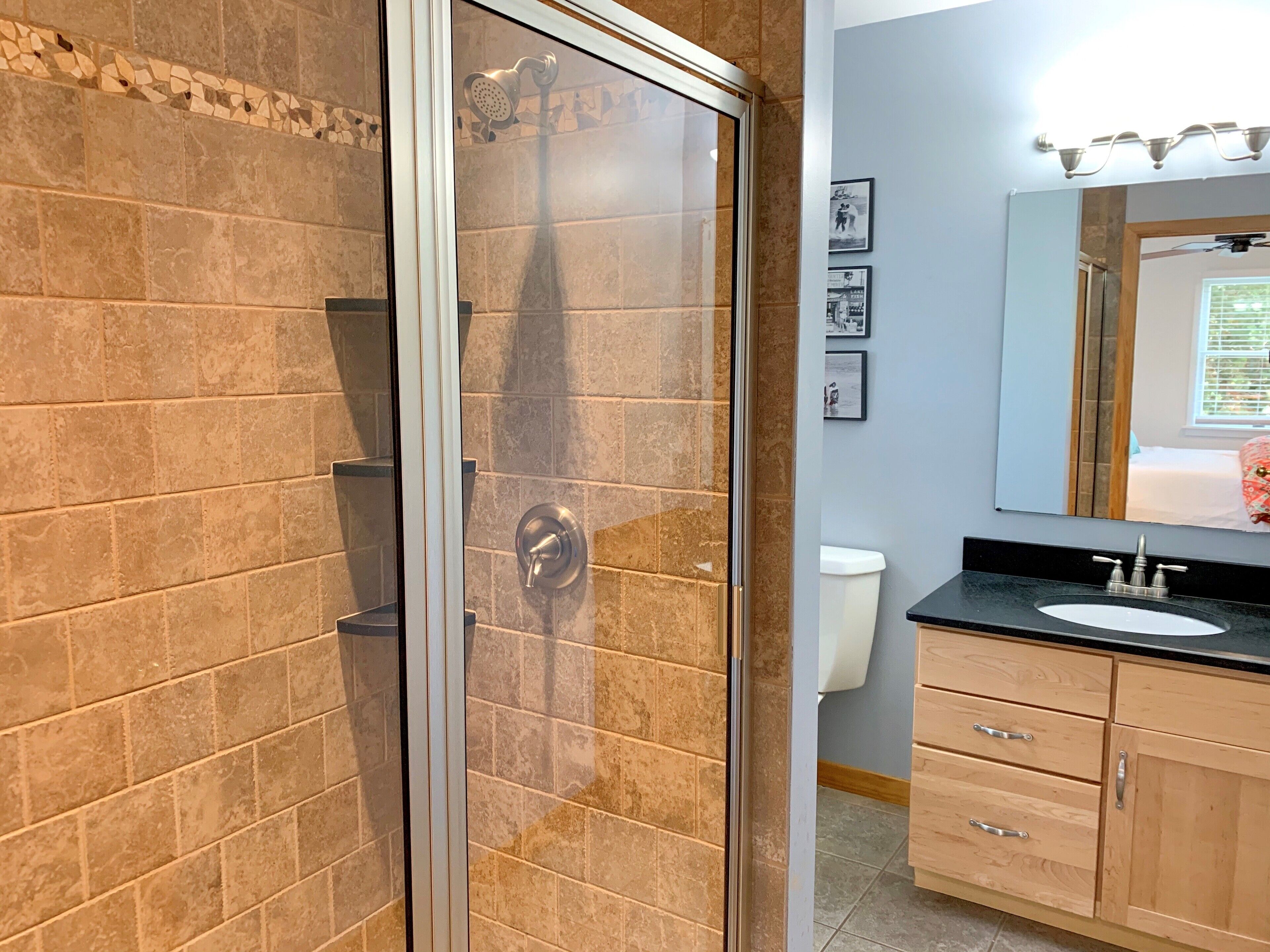 Une salle de bain dotée d’une douche à parois de verre, d’un lavabo avec un plan de travail noir, de meubles en bois et d’un miroir au-dessus du lavabo.