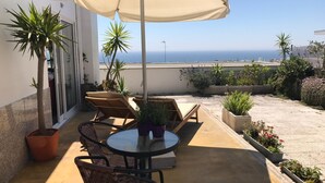 Een terras met een ronde tafel, twee loungestoelen en een grote parasol.