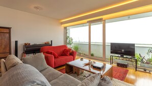 Een moderne woonkamer met een rode bank, een grijze bank en een houten salontafel. Een flatscreen televisie staat op een dressoir, en er staat een piano op de achtergrond.
