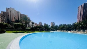 A swimming pool with a clear blue water surface, surrounded by a green lawn and palm trees. - A45 - Fantastic urbanization close to the beach (Cala de Finestrat)