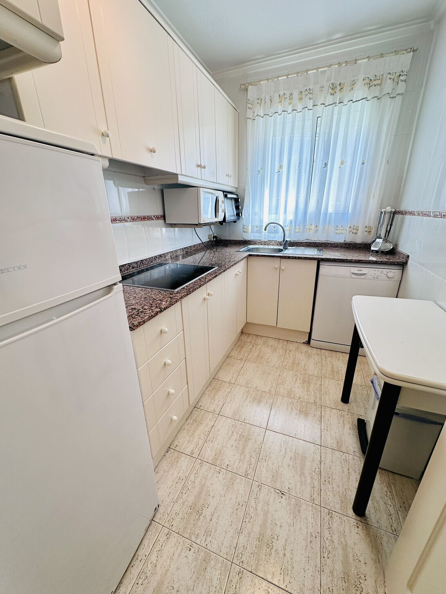 A compact kitchen with white cabinets, a granite countertop, a built-in microwave, a sink, and a small table.