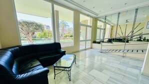 A spacious lobby with a black leather sofa, a glass coffee table, and a view of a staircase and outdoor greenery. - A45 - Fantastic urbanization close to the beach (Cala de Finestrat)