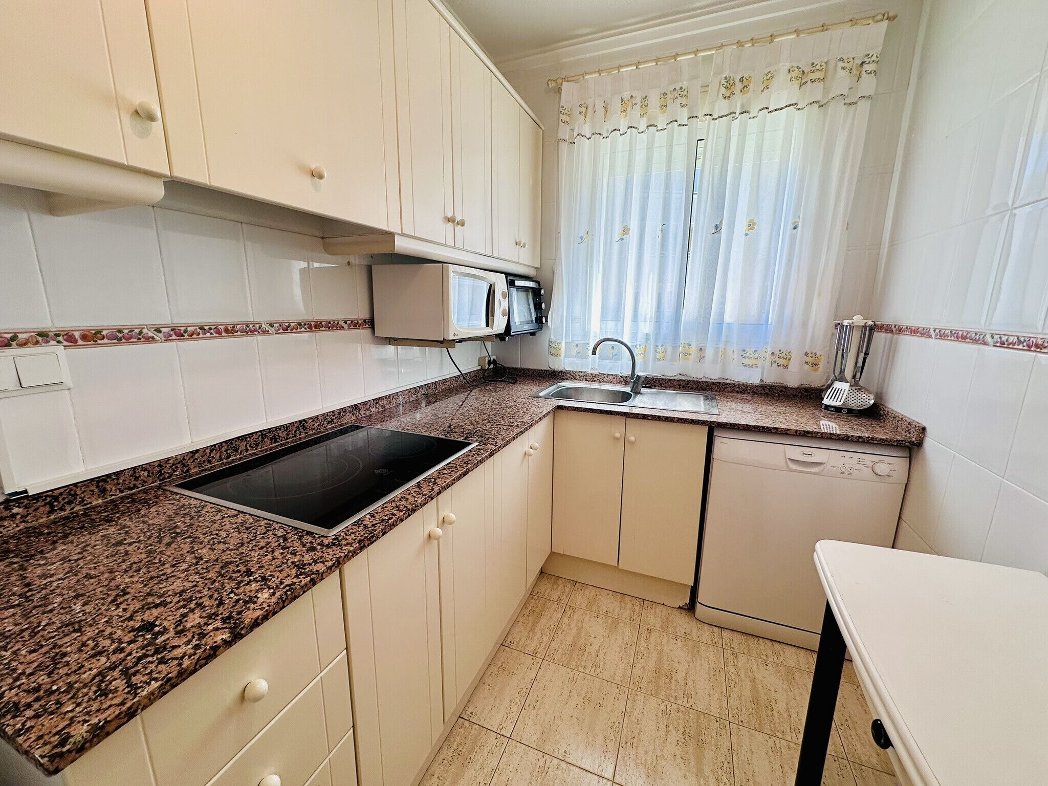 A compact kitchen with white cabinets, a granite countertop, a built-in microwave, a sink, and a dishwasher.