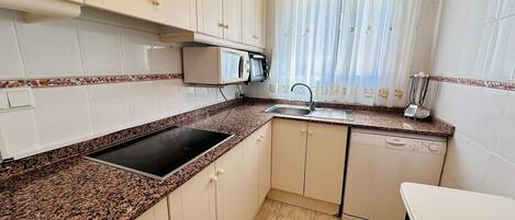 A compact kitchen with white cabinets, a granite countertop, a built-in microwave, a sink, and a dishwasher.
