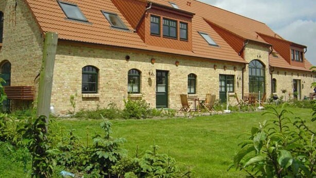 A two-story building with a sloped roof, multiple windows, and a well-maintained lawn. - 07 Holiday apartment - holiday farm on Rügen (Putbus)