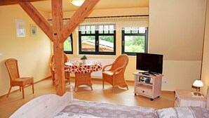 A room with a bed, a dining table with chairs, a television, and a window with curtains. - 07 Holiday apartment - holiday farm on Rügen (Putbus)