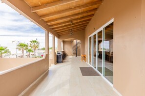 A covered outdoor corridor with a view of the sea, a staircase, and a dining area.