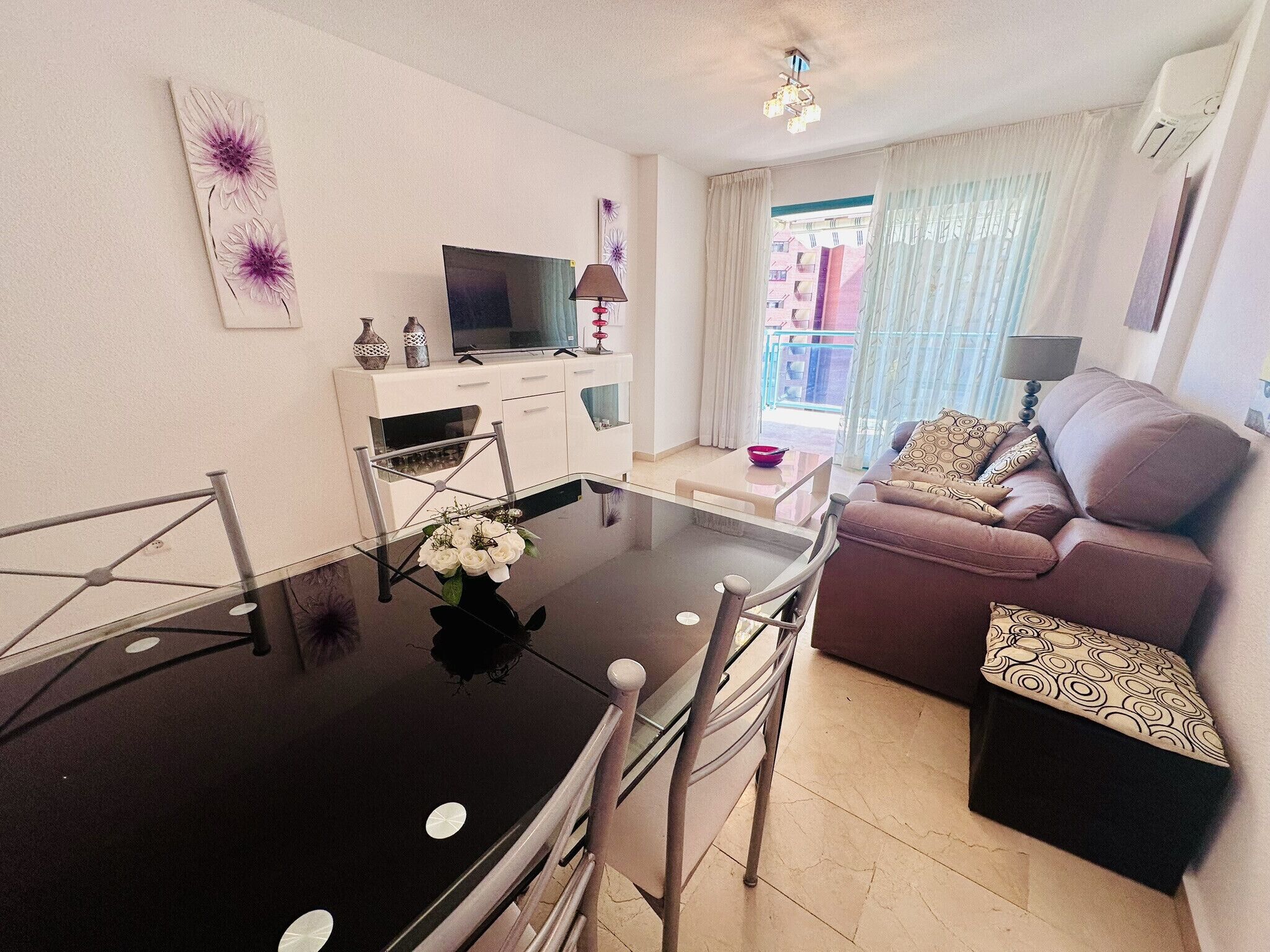 Een moderne woonkamer met een glazen eettafel, een bank en een televisie op een witte kast.