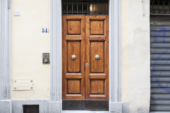 Uma porta de madeira dupla com uma tranca de metal, uma pequena janela acima e o número '54' na parede.