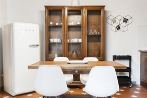 A dining area with a wooden table, white chairs, a white refrigerator, and a wooden cabinet with glass doors.