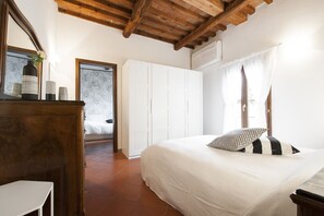 A bedroom with a bed, a wardrobe, a mirror, and a door leading to another room.